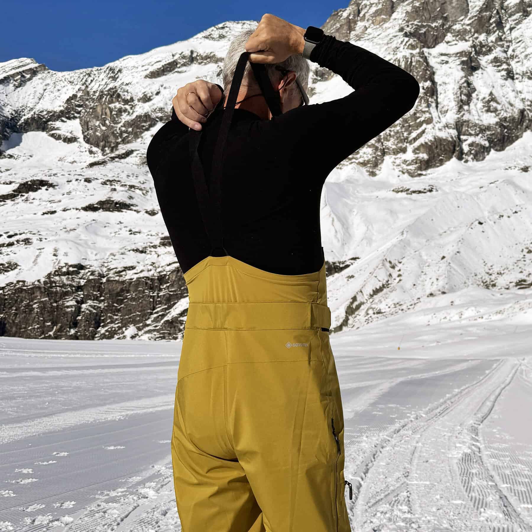 Scarponi da sci uomo in montagna con abbigliamento tecnico e paesaggio innevato.